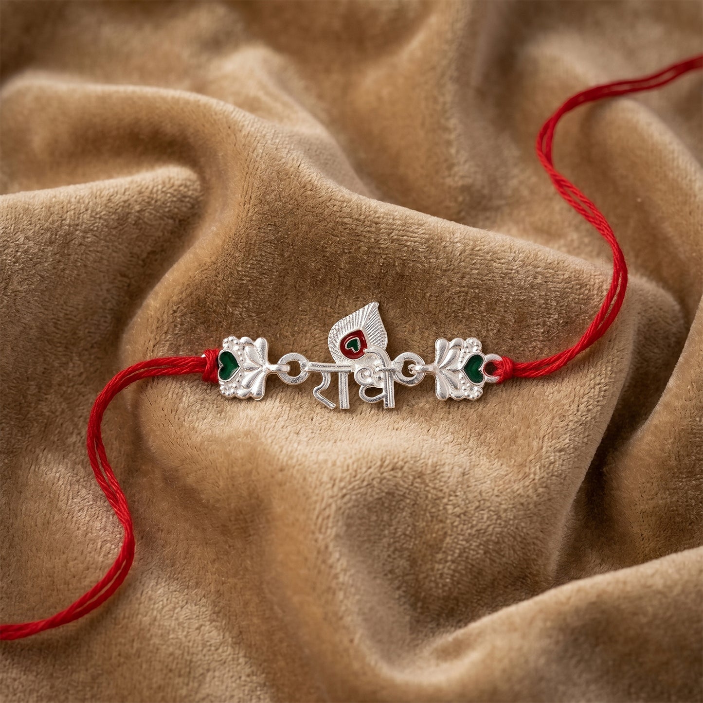 Silver Radhe Morpich Text Rakhi with Green Stones and Red Thread