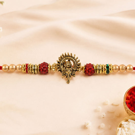 Close-up of Ganesh Ji Rakhi with antique gold, red beads, and pearl-style accents.