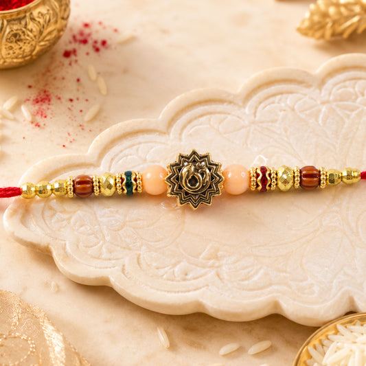 Golden Om Rakhi with peach beads and red thread in a close-up view.