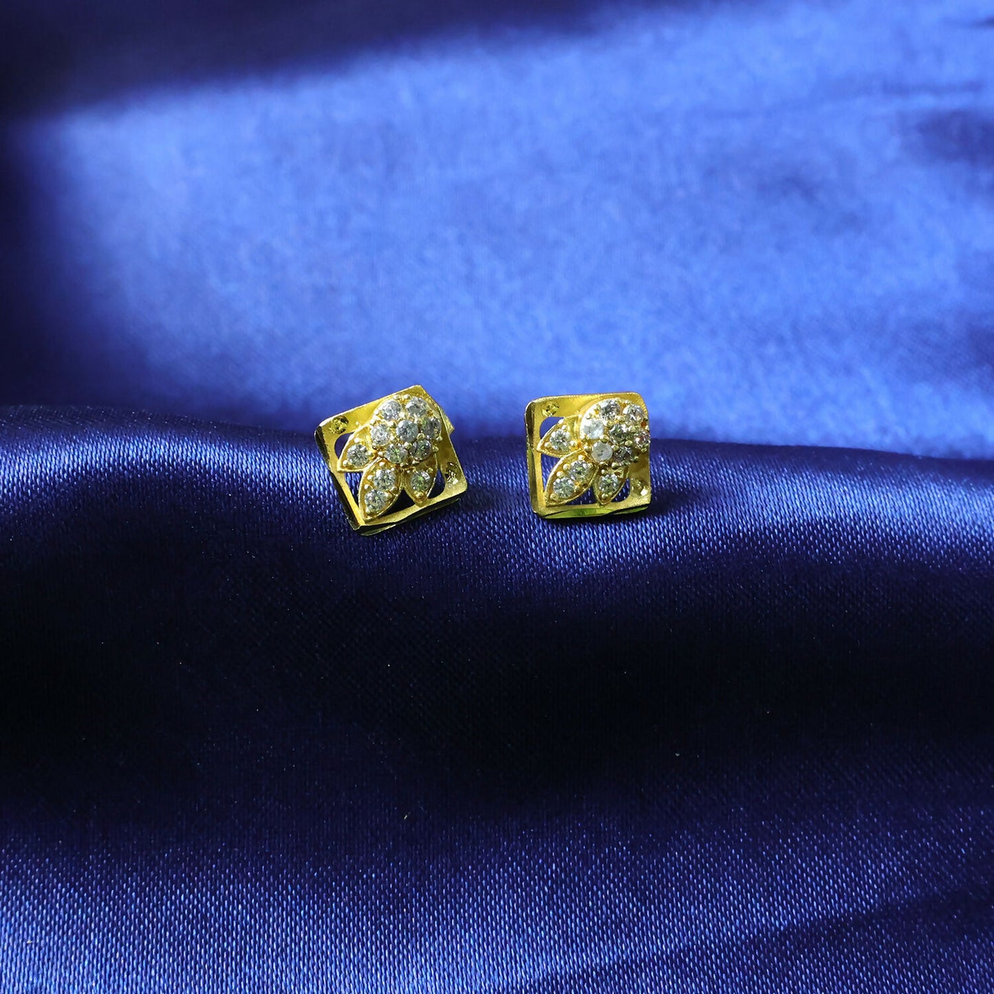 Detailed view of floral design on gold stud earrings with sparkling stones