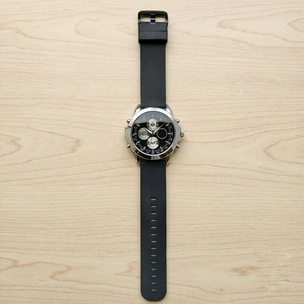 Top-down view of a black silicone strap watch with a silver case and black dial, on a light wood surface.
