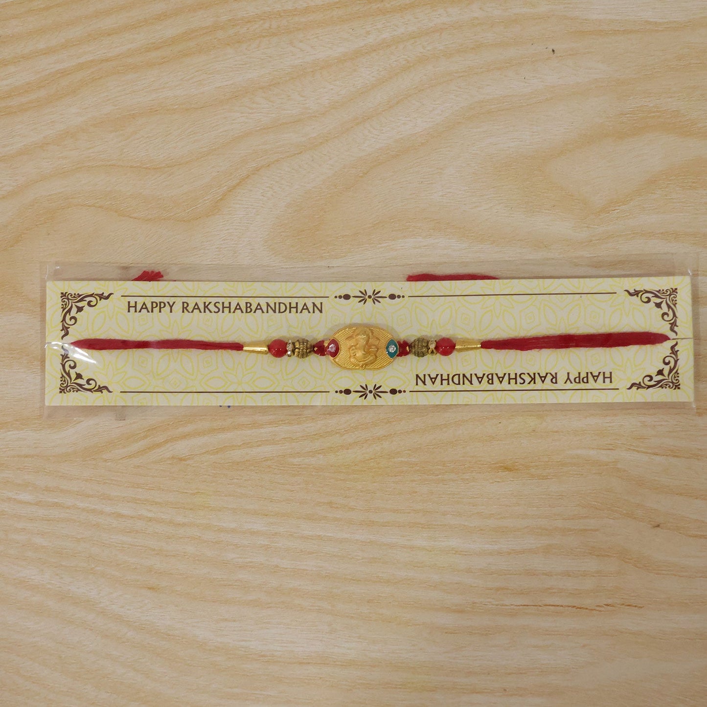 Hand holding Lord Ganesha gold-plated rakhi with red beads