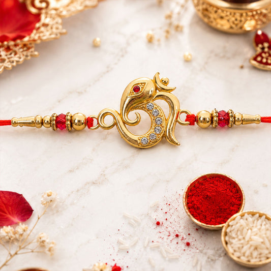 A gold-toned Om Ganesha charm with clear stones and a red bead eye, on a red thread with gold and red beads, surrounded by
