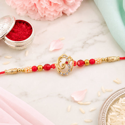 A gold-toned Ganesha charm with clear crystals and red beads on a red thread, surrounded by pink flowers and white rice