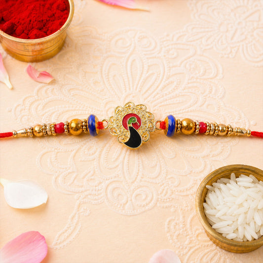 A gold-toned peacock charm with red, green, and black enamel is centered on a red thread with gold, blue, and red beads,