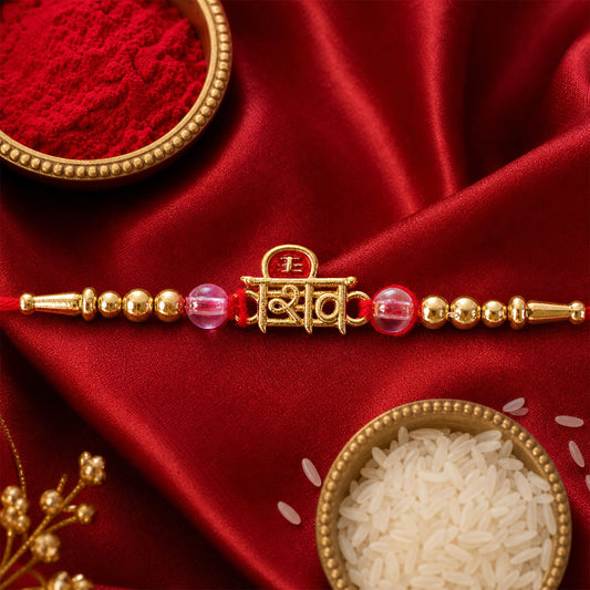 A red thread with golden beads and pink glass charms, centered by a golden Shiv charm, lies on a red satin cloth with rice
