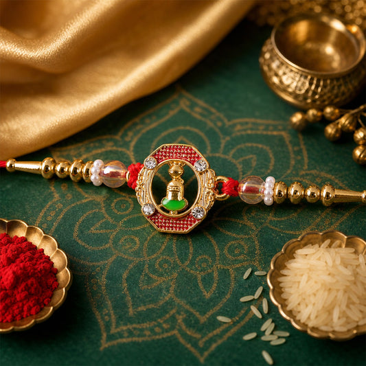 A red and gold Shivling charm with clear beads and gold accents rests on a green patterned fabric with red powder and rice.