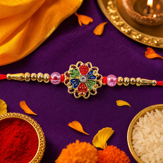 A vibrant Rakhi with a gold floral center, colorful enamel petals, and pink and gold beads, on a purple cloth with festive