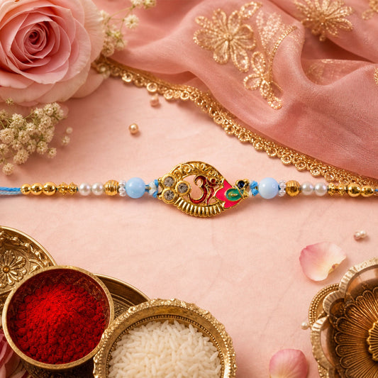 A gold Om motif with pink and green enamel is centered on a light blue thread with pearl and gold beads, on a pink