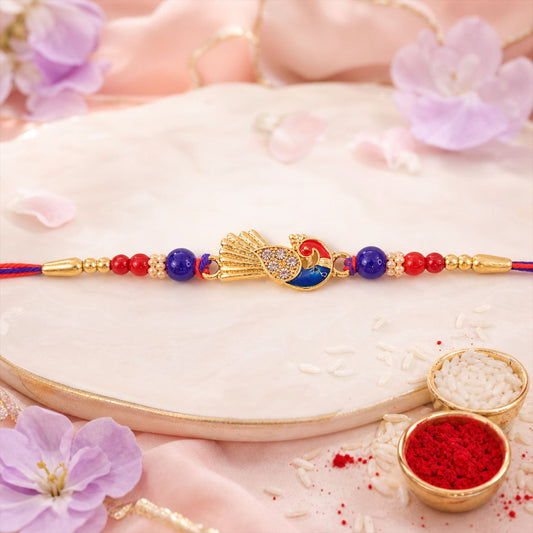 A gold peacock charm with blue and red enamel, flanked by red and blue beads, rests on a white plate with rice and red