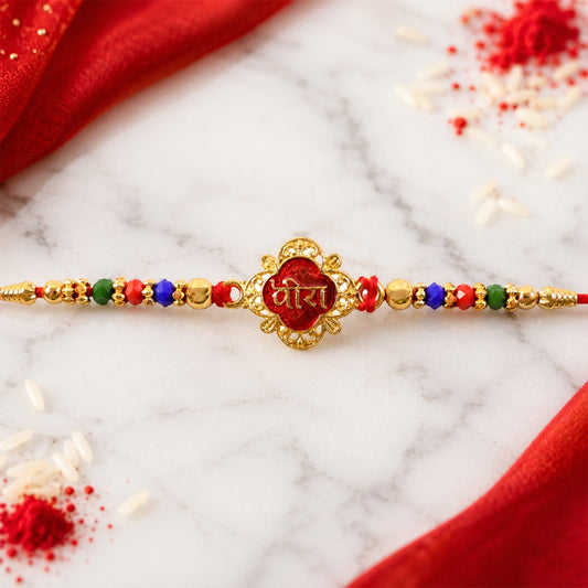 A red and gold bracelet with a central red enamel charm and colorful beads rests on a marble surface with red fabric, rice,