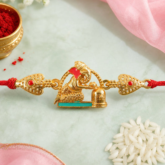 A gold-colored Ganesh figure with red and teal enamel sits on a red thread, flanked by filigree hearts with red stones.
