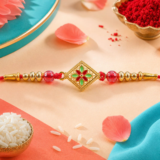 A red-threaded bracelet with a square gold-toned floral centerpiece and red beads is displayed with rice and rose petals.