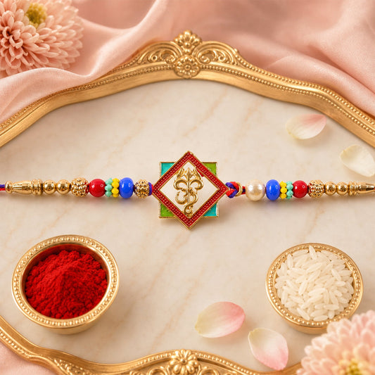 A colorful Om Symbol and Trishul Rakhi is displayed on a pink silk cloth, with small bowls of rice and red powder nearby.