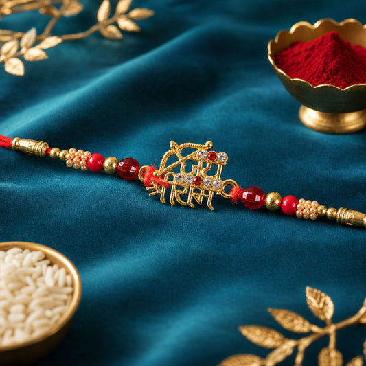 A gold-colored Jai Shree Ram charm with a bow and arrow, adorned with red and clear stones, on a red thread with red and
