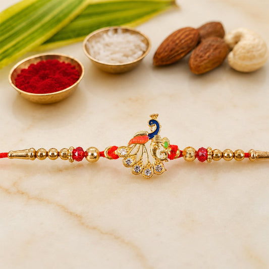 A red thread bracelet with a gold peacock charm, red beads, and gold beads is displayed with almonds and cashews.