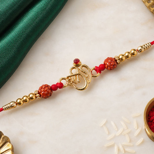 A red thread bracelet with a gold Om charm, red textured beads, and small gold beads is displayed on a white marble surface