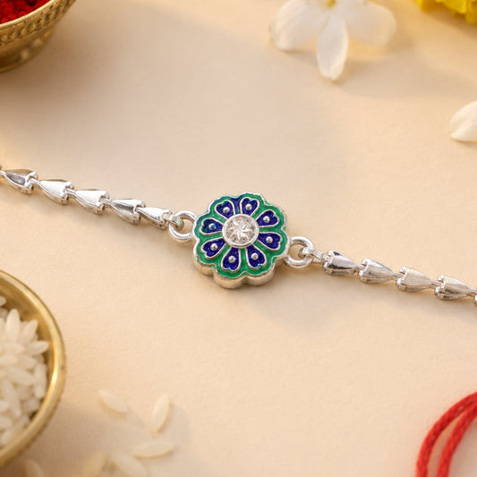 A silver chain bracelet features a central green and blue floral charm with a clear stone, on a light background with rice