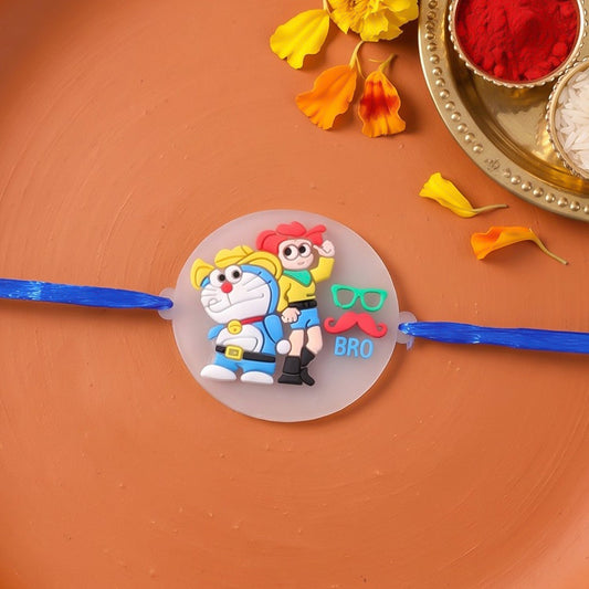 Blue Doraemon and Nobita Rakhi with a 'BRO' charm, set on an orange surface with yellow flowers and puja thali items.