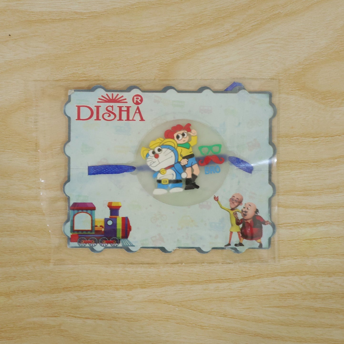 The Doraemon and Nobita Rakhi with a 'BRO' charm, packaged in a clear plastic sleeve with a DISHA branded card.