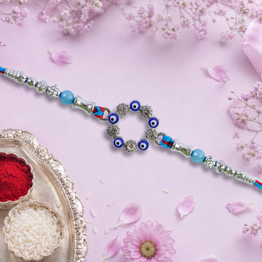 A blue and red thread rakhi with a circular evil eye charm, silver and turquoise beads on a pink floral background.