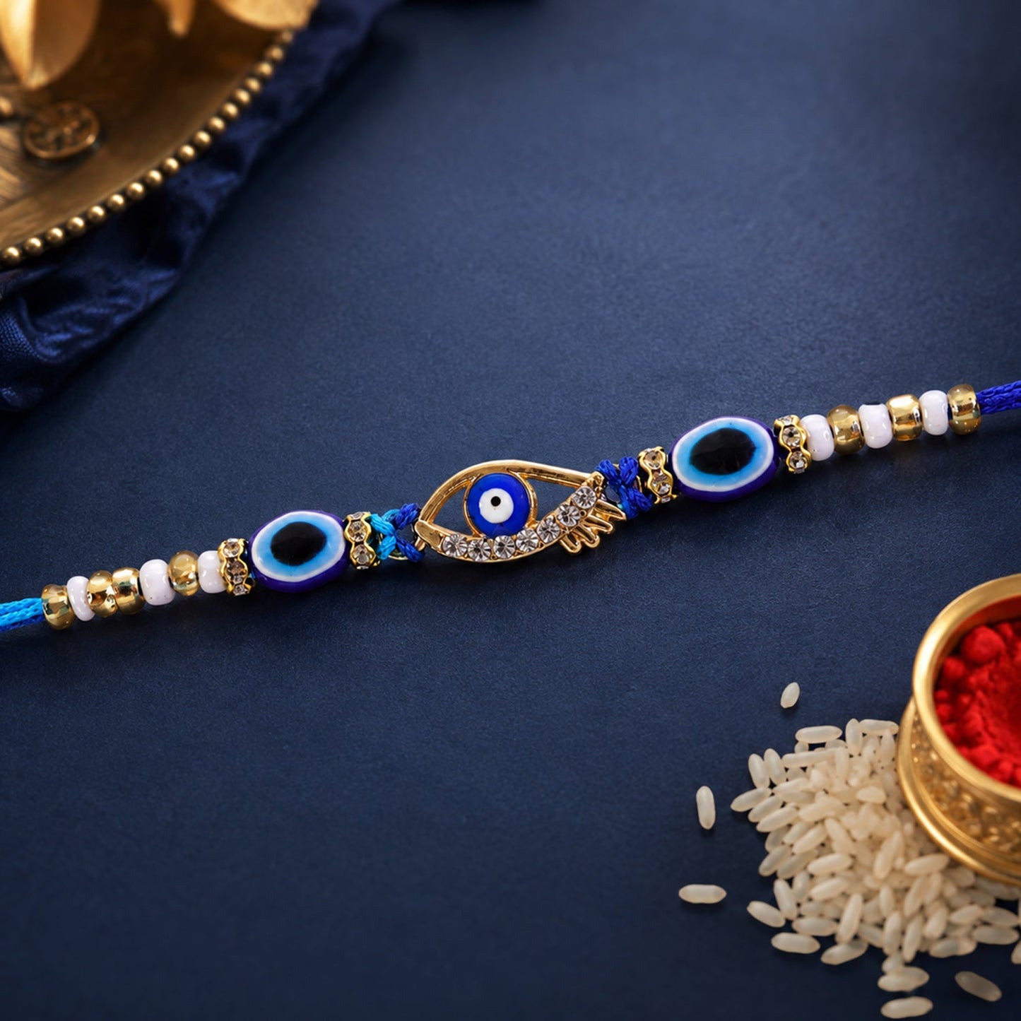 A blue evil eye rakhi with a gold and rhinestone center charm, accented with smaller blue evil eye beads and white and gold