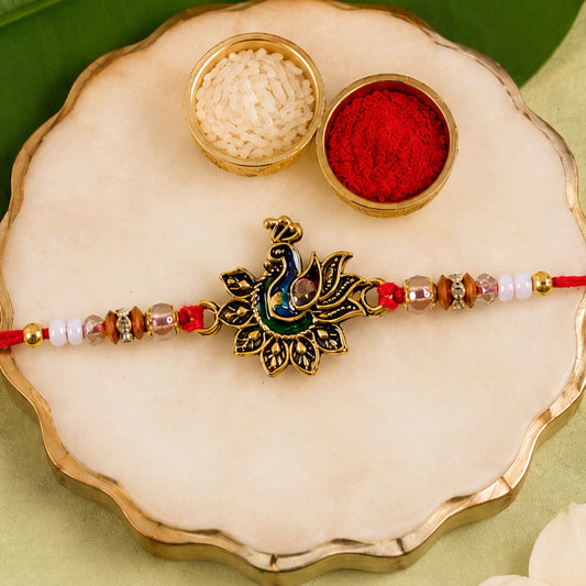Close-up view of Peacock Floral Golden Rakhi with blue green enamel and pearl beads on a red thread.