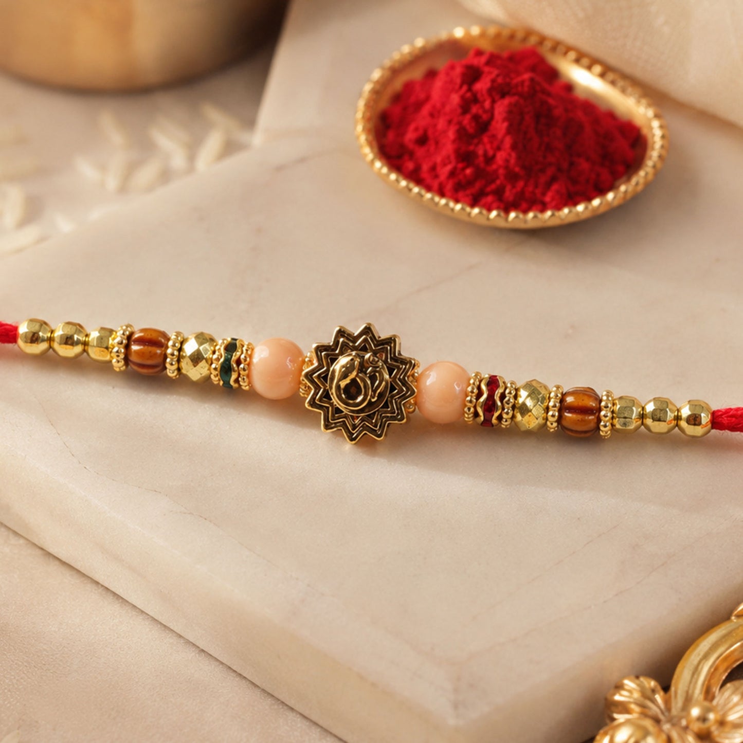 Om Sacred Symbol Golden Devotional Rakhi with Peach Beads and Red Thread
