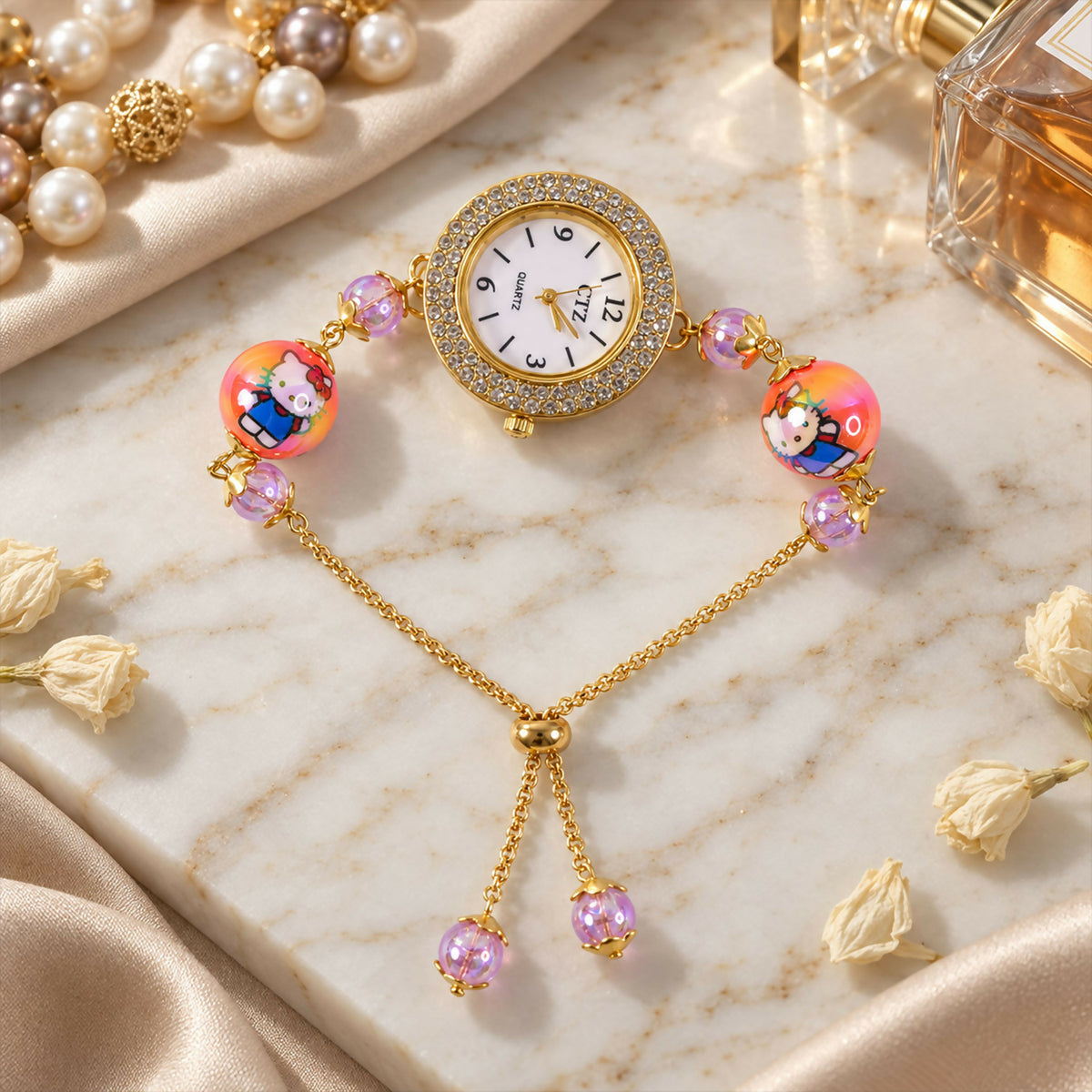 A gold-tone bracelet watch with a rhinestone-studded dial, two orange cartoon character beads, and smaller purple beads,