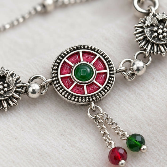 Close-up of an oxidized silver bracelet with a red and green enamel mandala center and floral links.