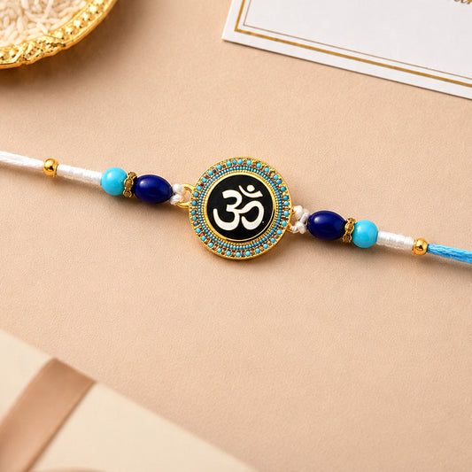 A gold and black Om symbol charm is centered on a white and blue braided thread, flanked by blue beads.