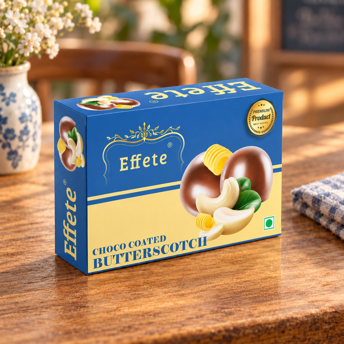 A blue and beige box of Effete Choco Coated Butterscotch sits on a wooden table with a vase of white flowers.
