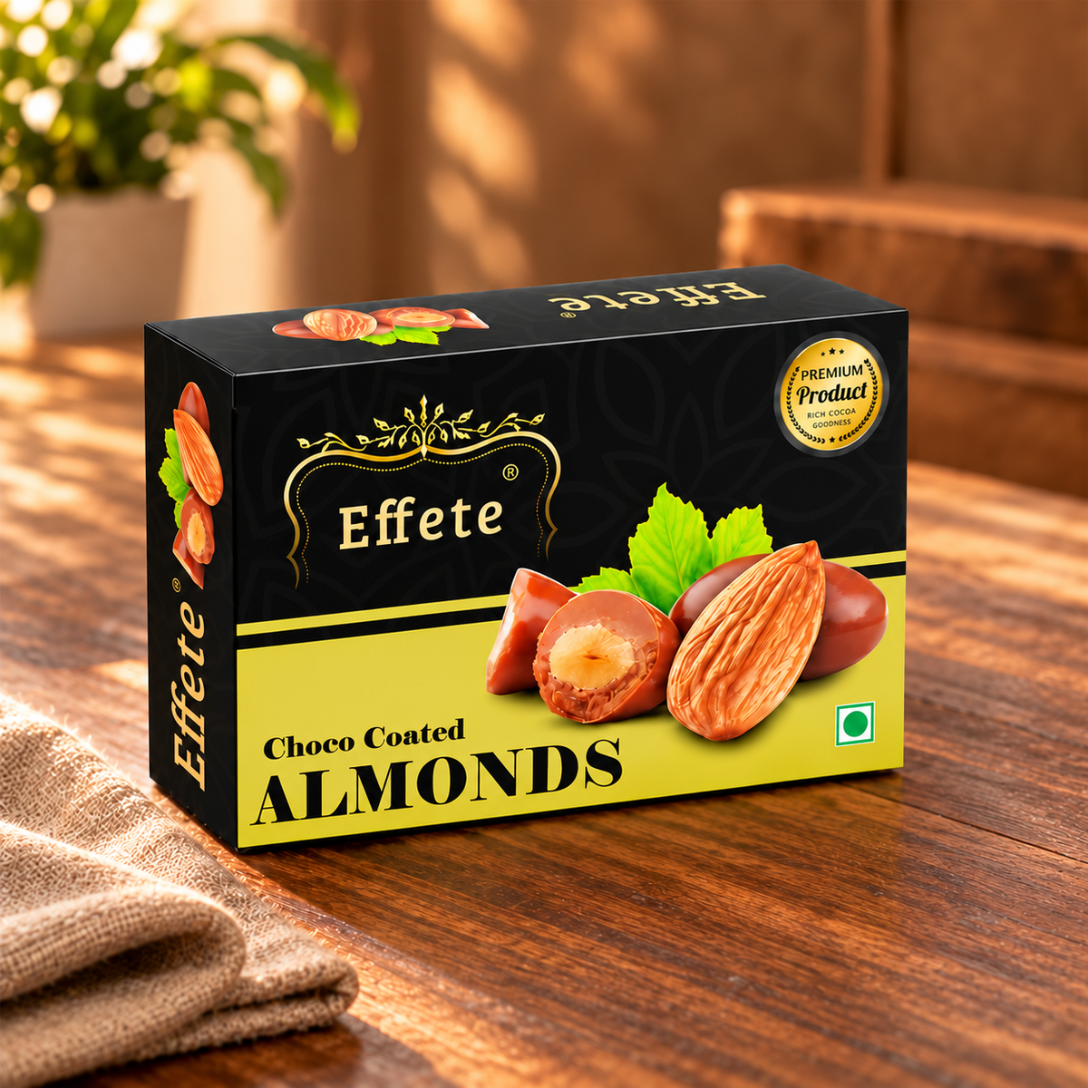 A black and yellow box of Effete Choco Coated Almonds sits on a wooden table with a brown cloth napkin.