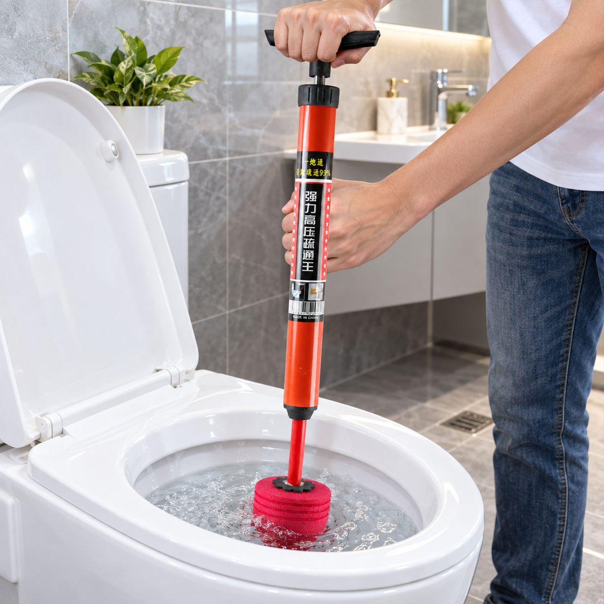 A person holds an orange and red pump plunger, pushing it into a toilet bowl filled with water.