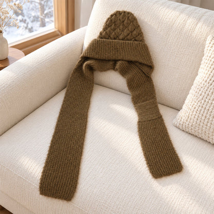 A brown knitted cap with an attached scarf is draped over a white textured sofa in a bright room.
