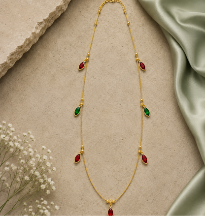 A delicate gold-plated chain necklace featuring alternating red and green marquise-cut crystal pendants, displayed on a