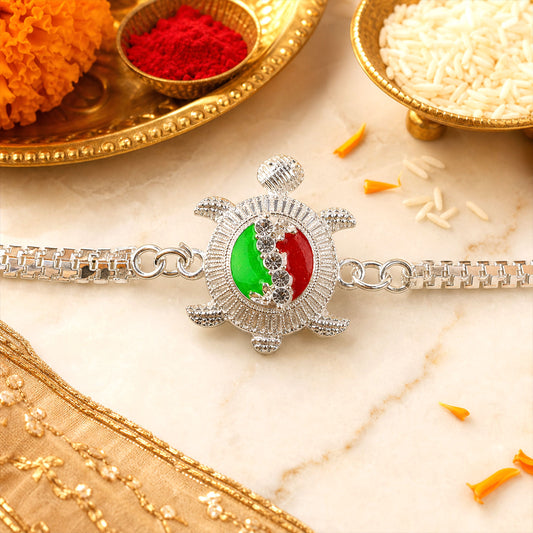 Silver Turtle Rakhi with red and green enamel detailing, presented on a decorative background.