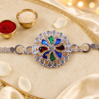 A silver chain bracelet with a round, colorful enamel and crystal centerpiece is displayed on a cream silk cloth with small