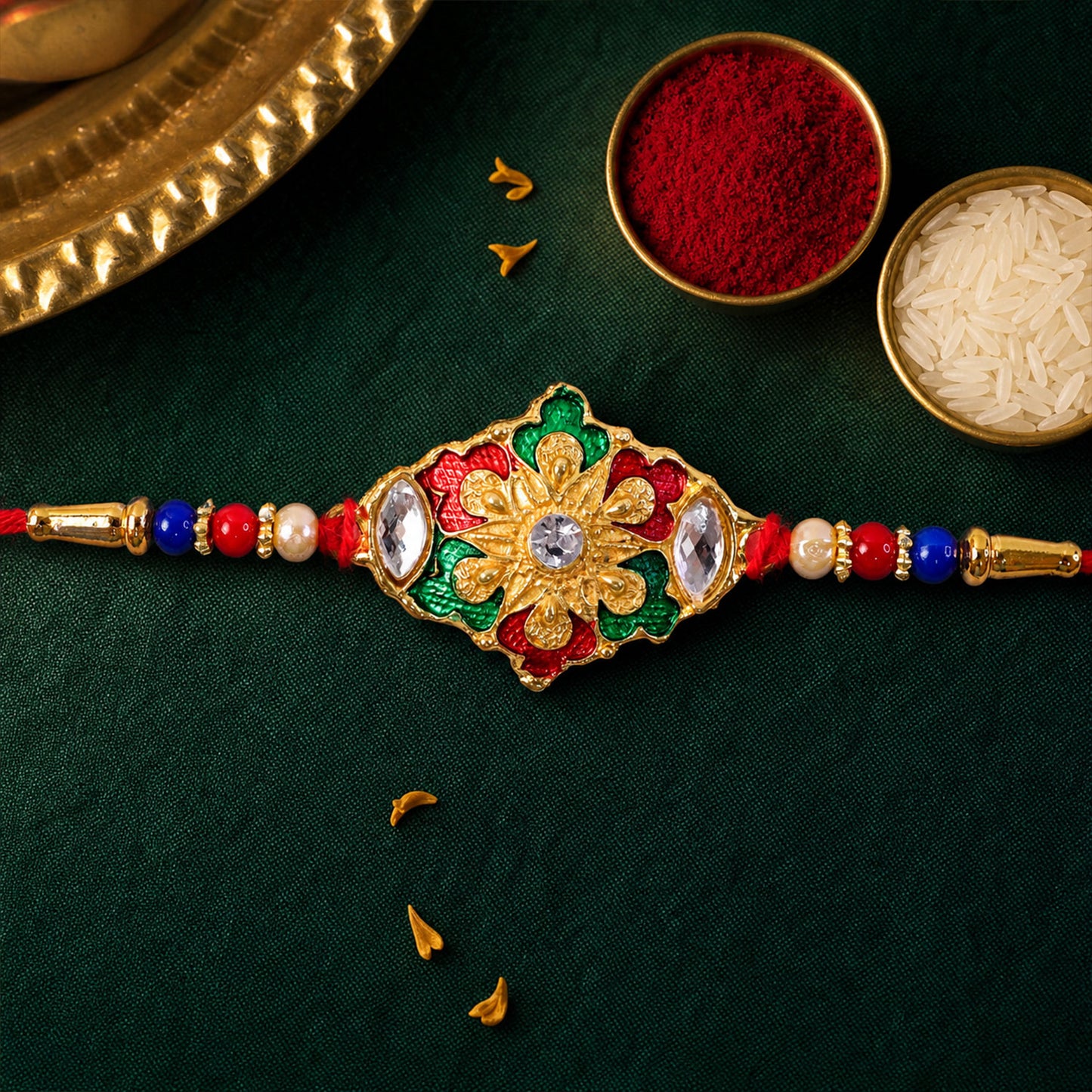 A gold-colored bracelet with a floral design, accented with red, green, and clear stones, resting on a dark green fabric.