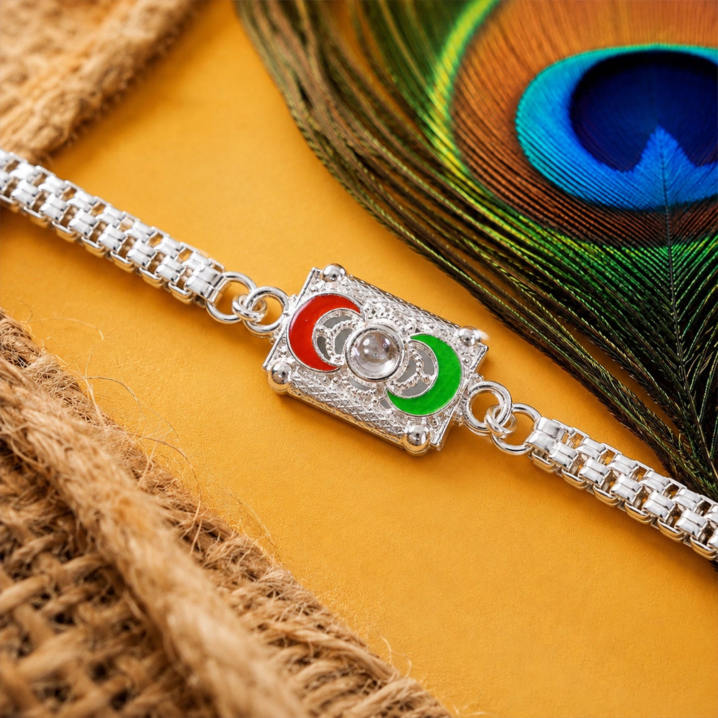 A silver-colored bracelet with a rectangular centerpiece featuring red and green crescent moon shapes, on a yellow surface