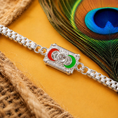 A silver-colored bracelet with a rectangular centerpiece featuring red and green crescent moon shapes, on a yellow surface