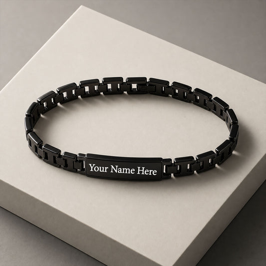 A black stainless steel link chain with a rectangular plate engraved with "Your Name Here" in white text, resting on a light