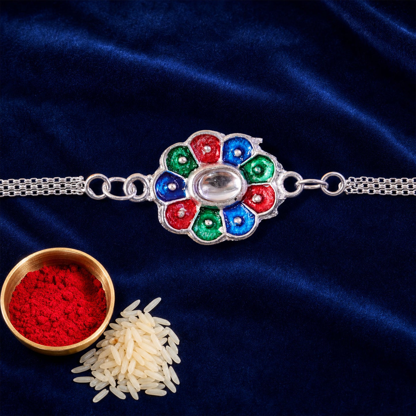 A silver chain bracelet with a colorful enamel flower charm rests on a dark blue velvet surface, accompanied by a small
