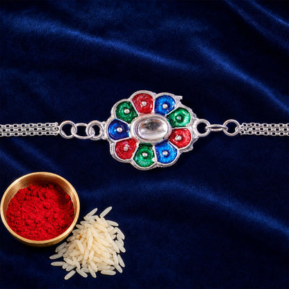 A silver chain bracelet with a colorful enamel flower charm rests on a dark blue velvet surface, accompanied by a small
