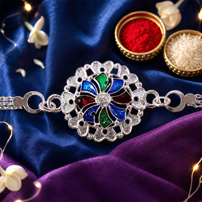 A silver chain bracelet with a round, colorful enamel and crystal centerpiece rests on dark blue and purple fabric,