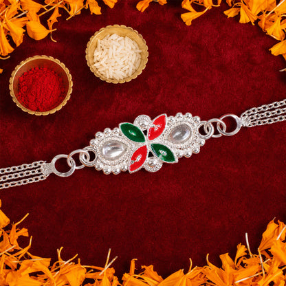 A silver-toned bracelet with a central floral motif in red and green enamel and clear stones is arranged on a rich red