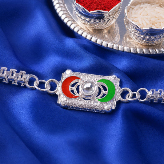 A silver-colored bracelet with a rectangular centerpiece featuring red and green crescent moon shapes, on a blue satin