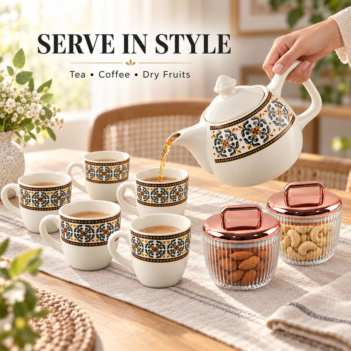 A hand pours tea from a white ceramic teapot into a cup, surrounded by five other cups and two jars with nuts.