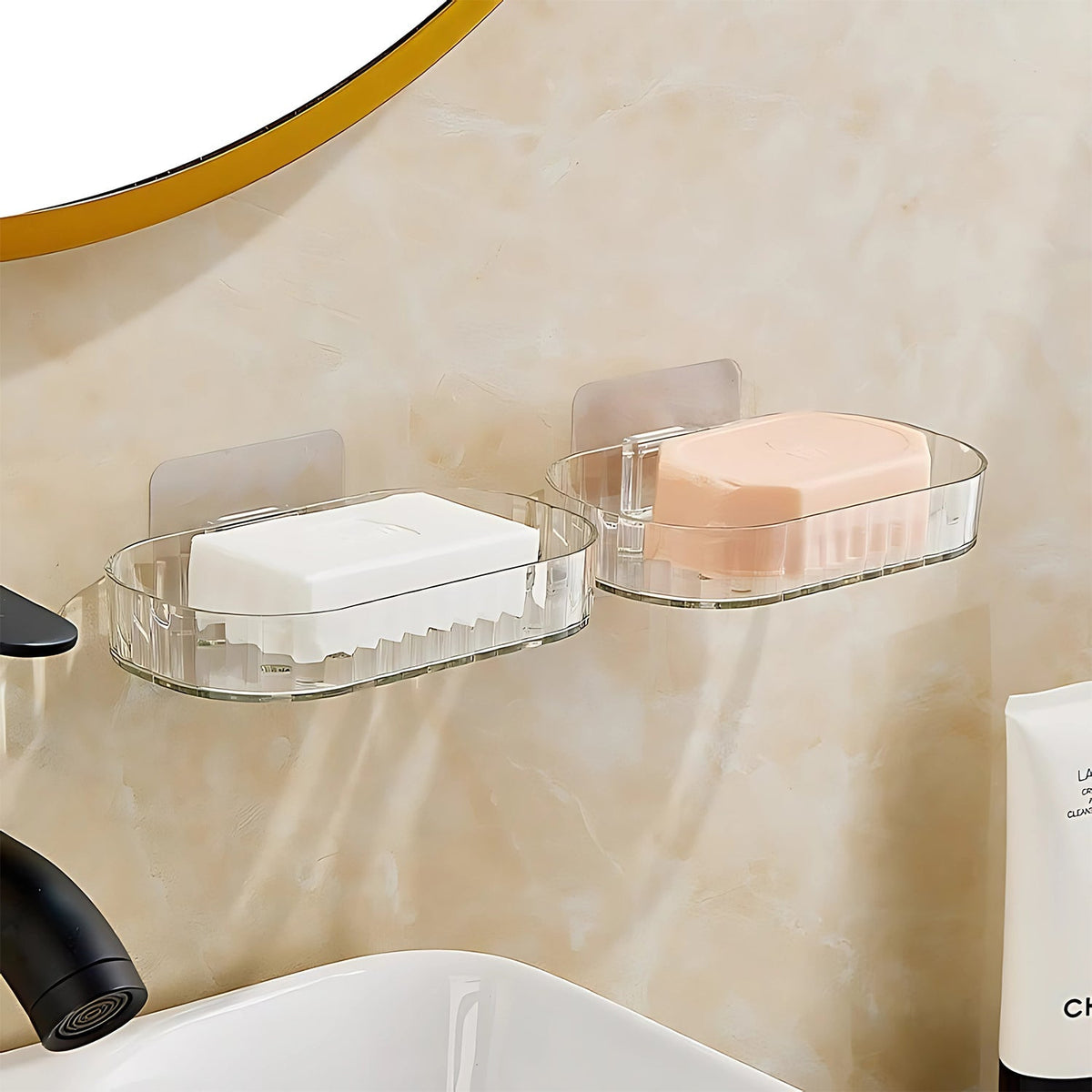 Two clear plastic soap dishes with white and pink soap bars are mounted on a marble wall.