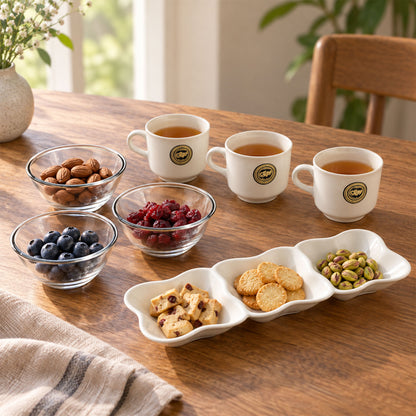Three white ceramic mugs with a light brown beverage, two clear glass bowls with almonds and blueberries, and a